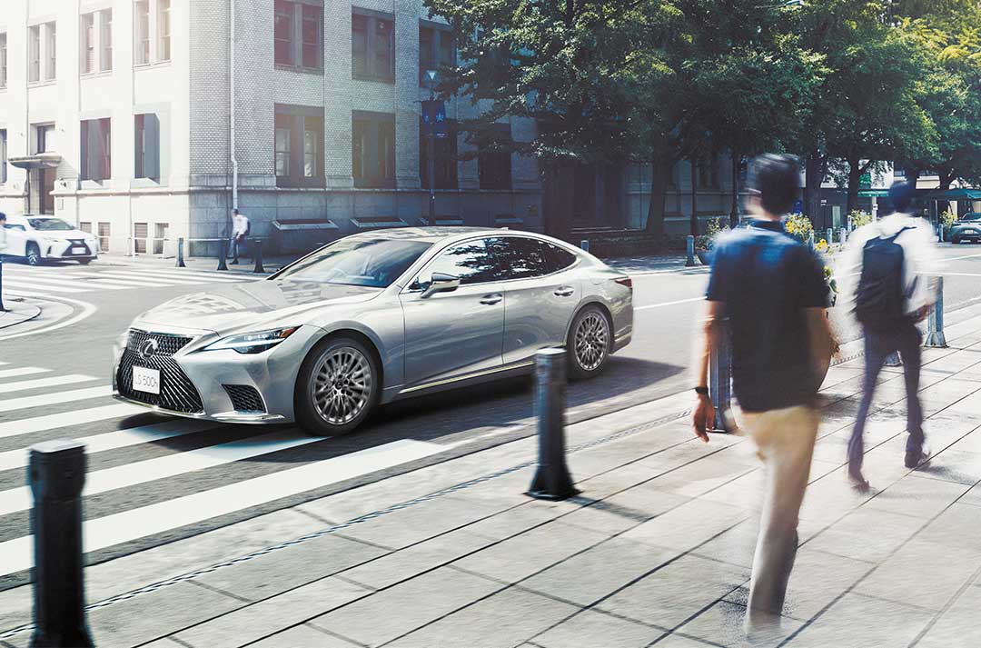 Silver Lexus LS is driven through city streets, pedestrians walk on the footpaths.