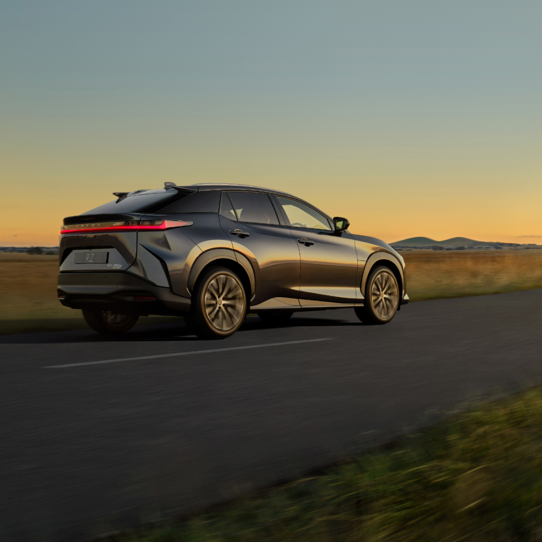 Rear side view of a Lexus RZ driving along an Australian country road as the sunsets.