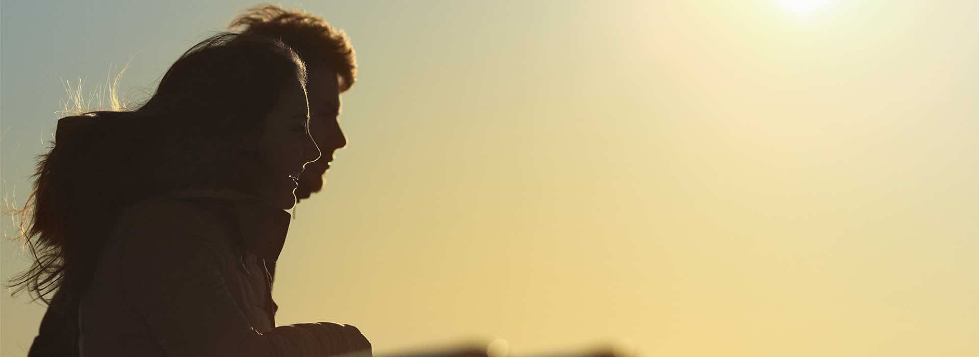 Shadowed man and woman with a yellow background, the wind blowing their hair.