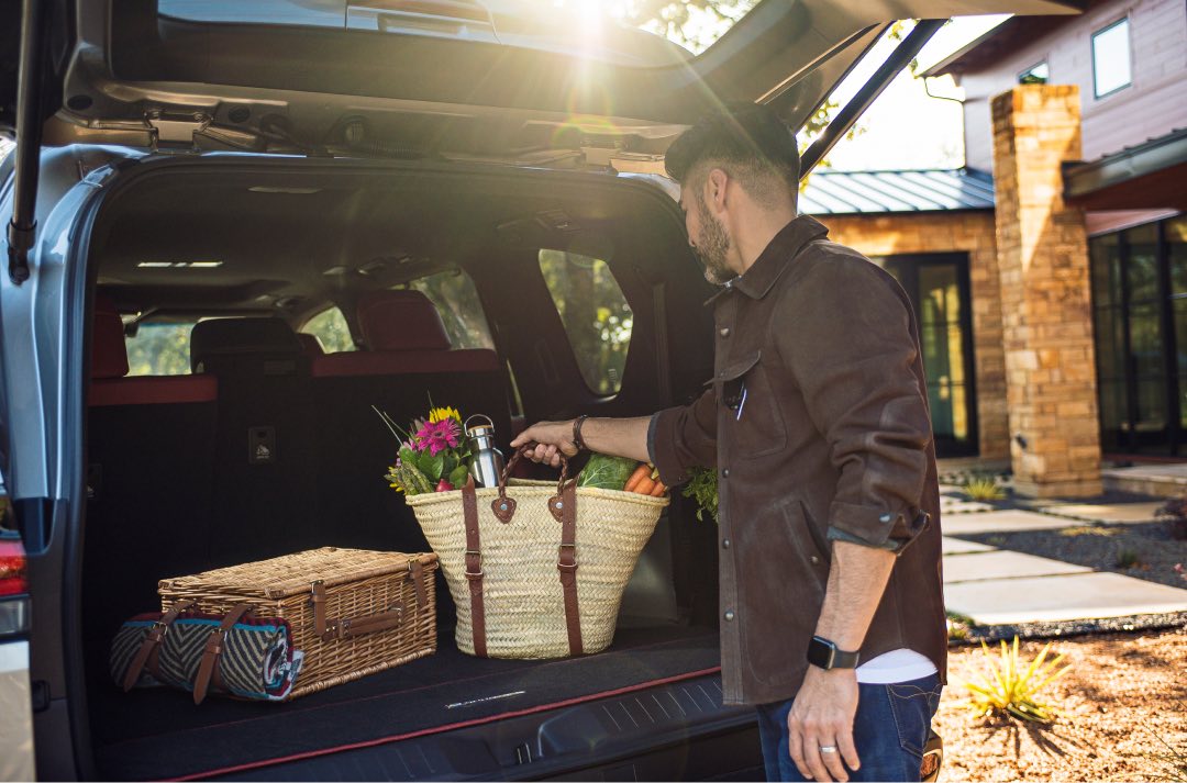 Man puts a whicker basket, filled with groceries and flowers, into the boot of a Lexus LX.