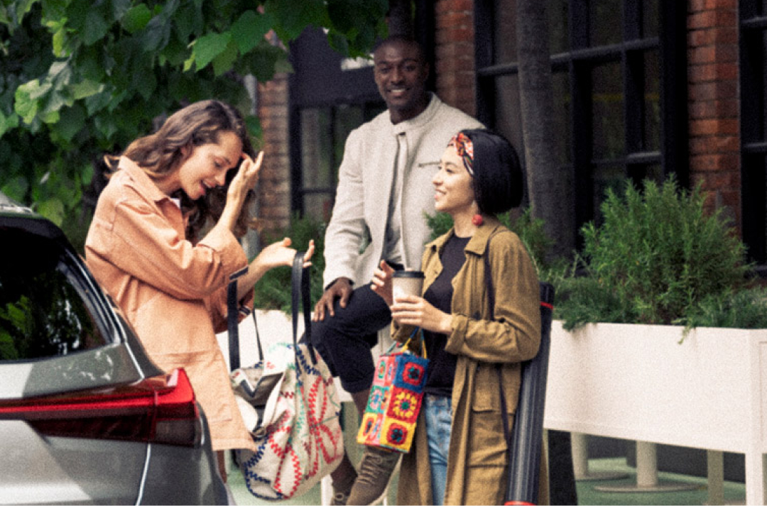 Two women and a man converse outside. They are all smiling.
