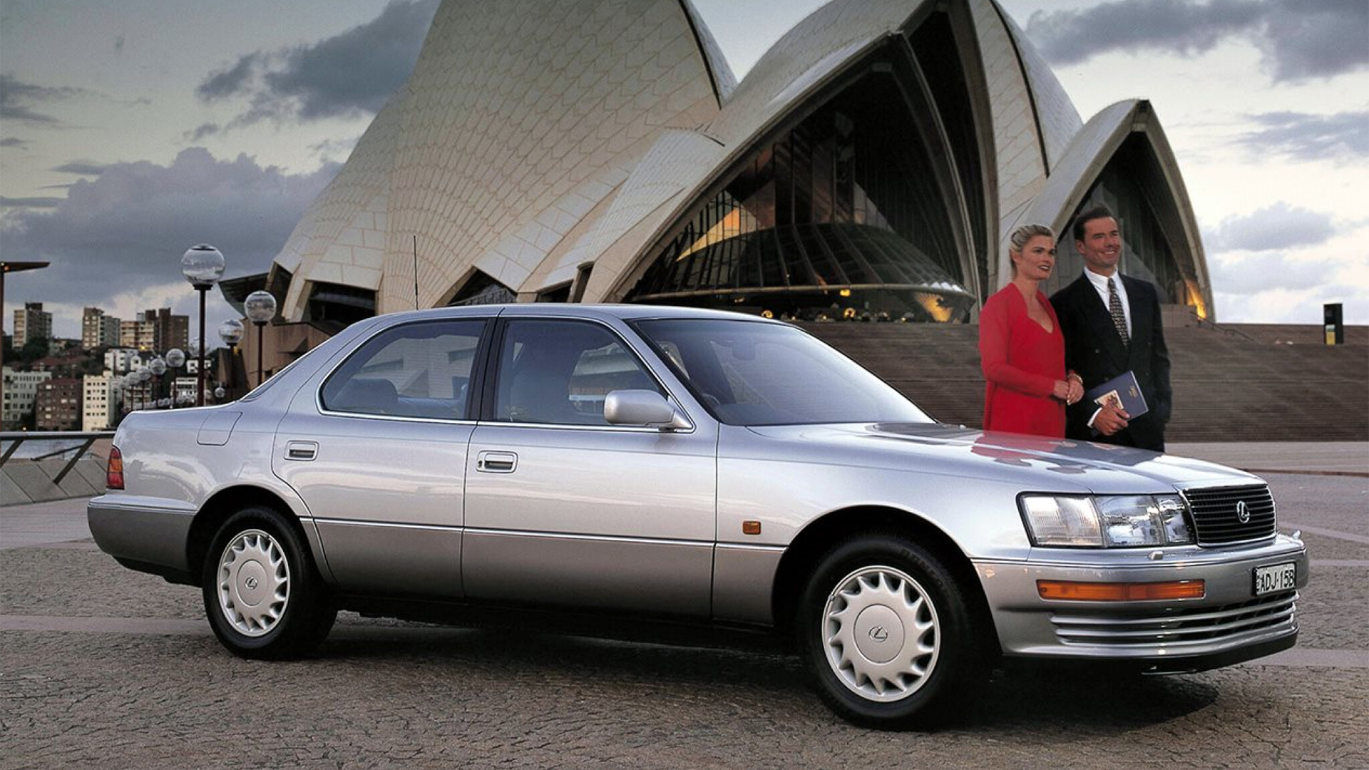 A man and woman stand with the first Lexus in front of the Sydney Opera House. 